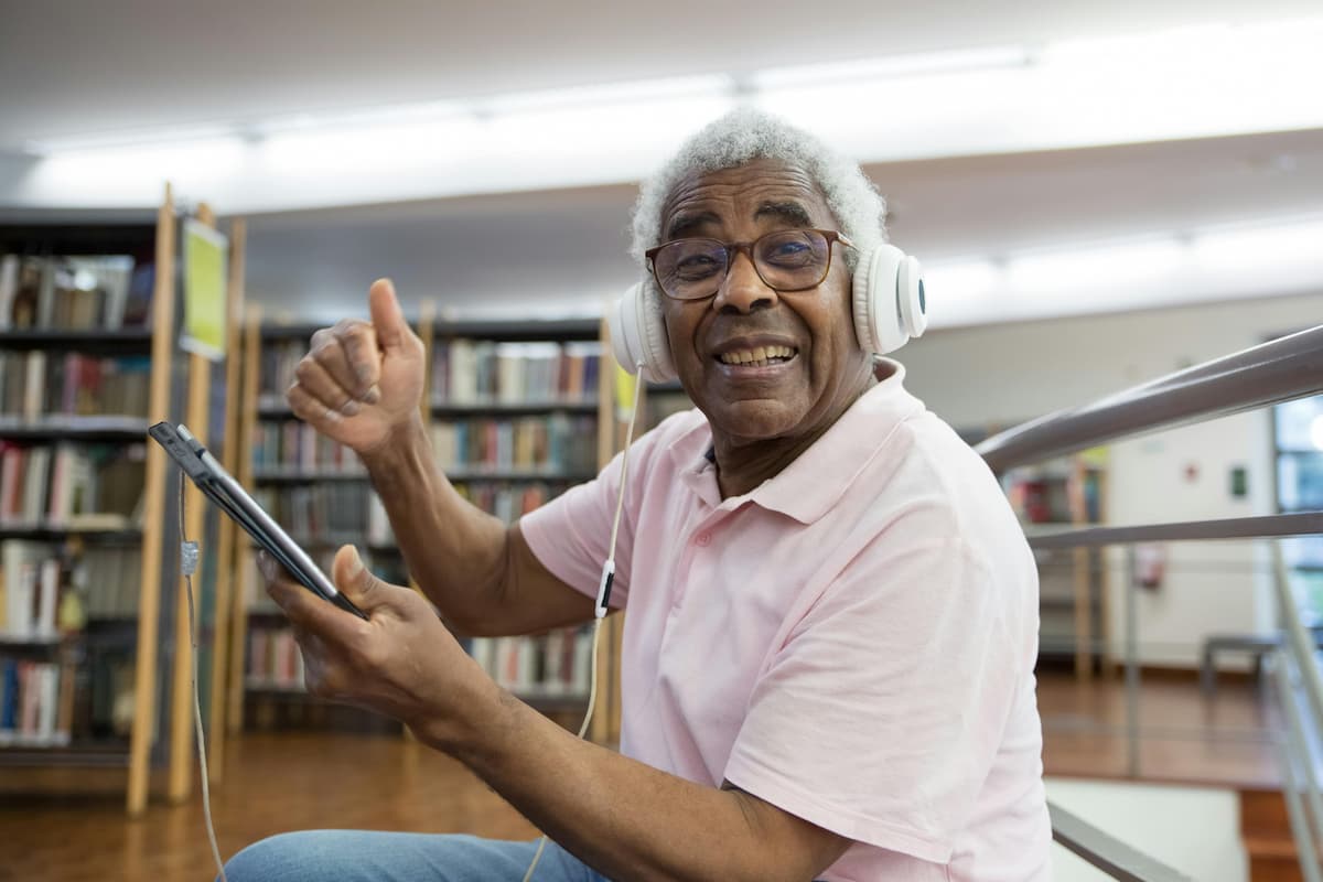 An older adult smiling and giving a thumbs up while using a tablet